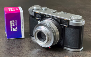 Die Kamera Lordox Baby der Firma Leidolf. Daneben steht ein verpackter Film Kentmere 400