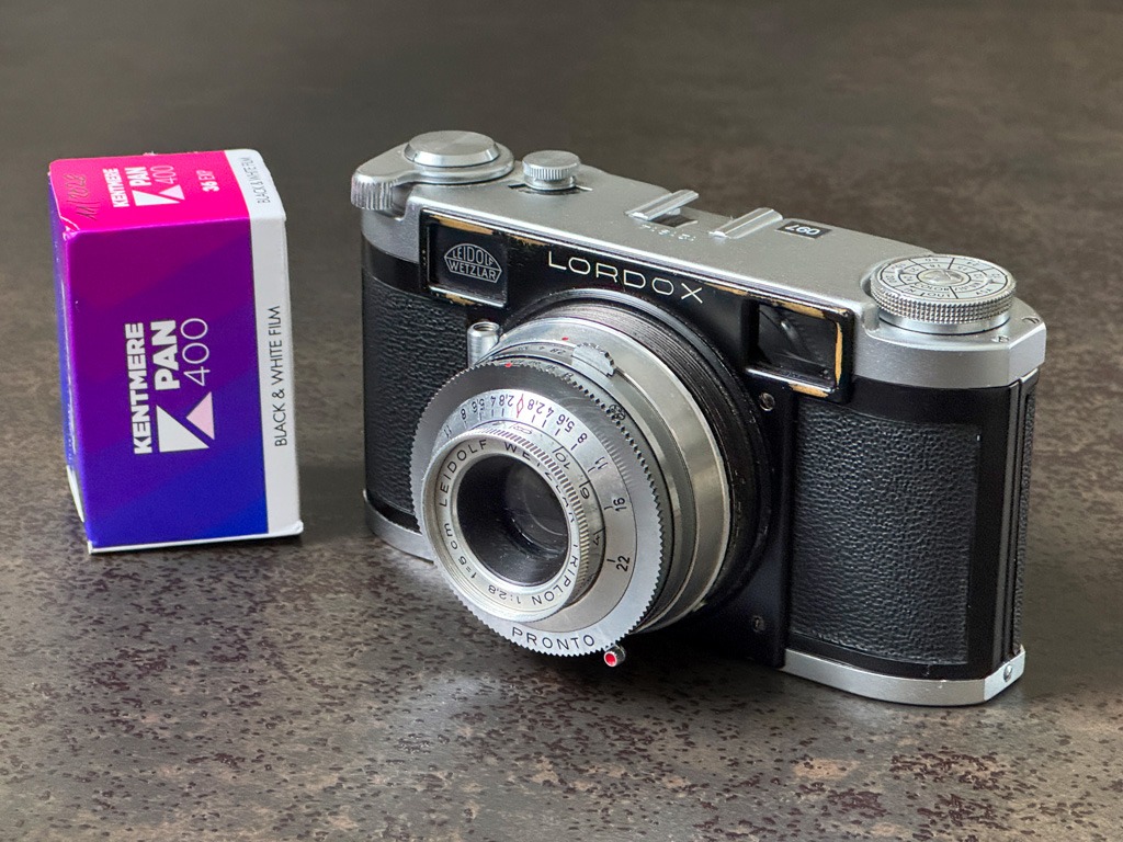 Die Kamera Lordox Baby der Firma Leidolf. Daneben steht ein verpackter Film Kentmere 400