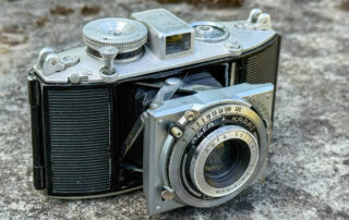Die Agfa Karat 3.5 steht mit ausgefahrener Ob jektivstandarte auf einer Mauer.