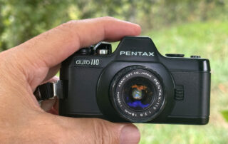 Die PENTAX auto 110 zwischen Daumen und Zeigefinter in der Hand gehalten.